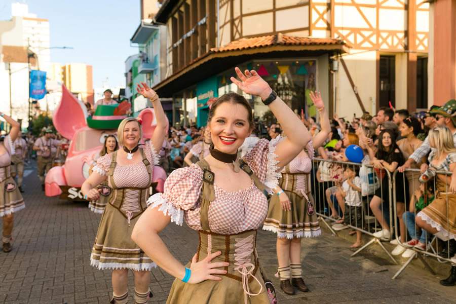 People celebrating Oktoberfest in Blumenau, Brazil, dressed in traditional German attire, enjoying beer, music, and festive decorations.