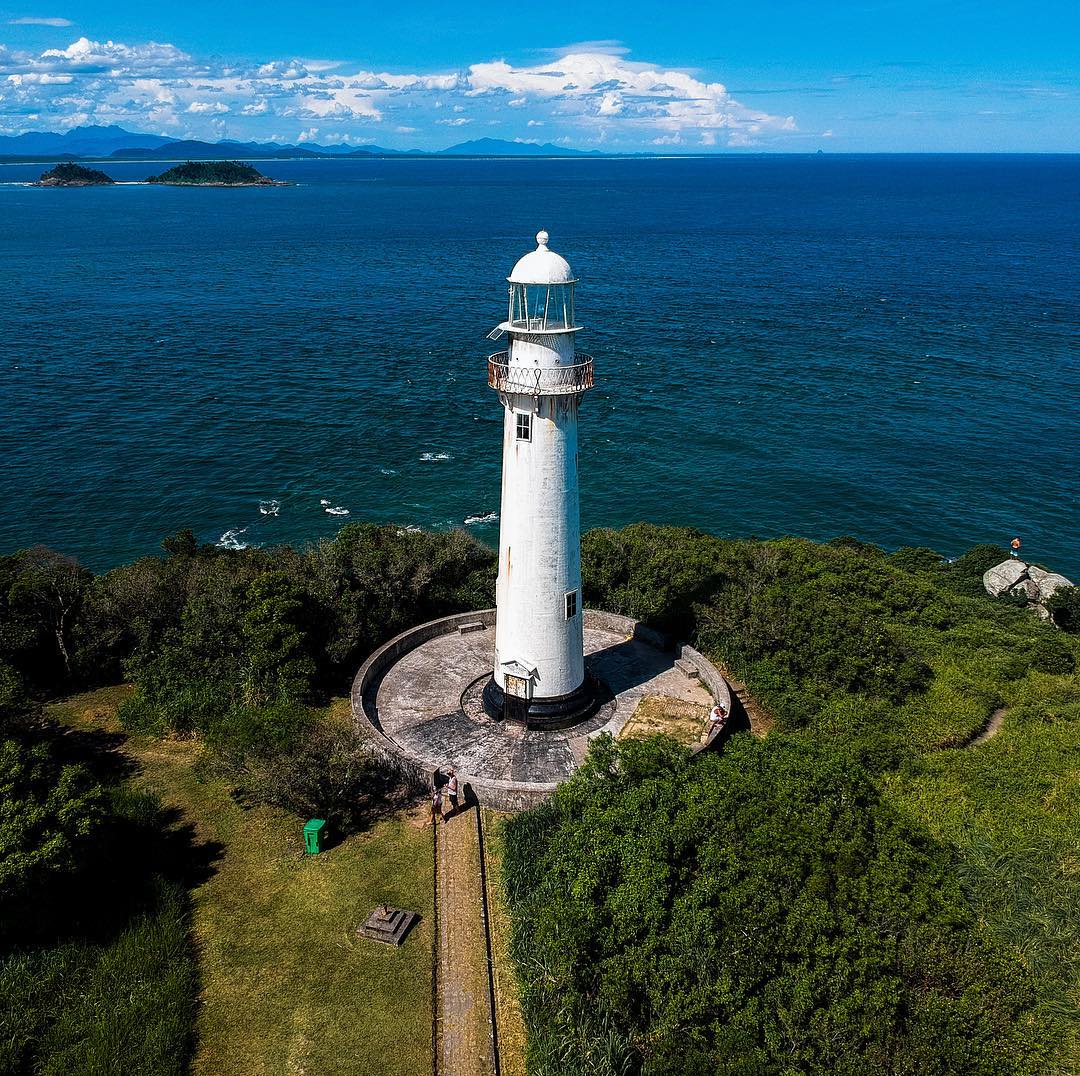 Stunning aerial view of Farol das Conchas on Ilha do Mel, Brazil, perched atop a green hill, overlooking the turquoise ocean.