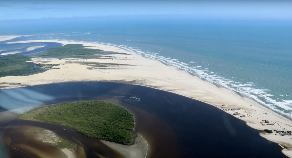 A scenic view of the Preguiças River flowing towards the Caburé Beach, with its peaceful waters and lush surroundings, offering a serene escape in the Lençóis Maranhenses region.