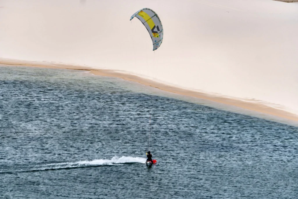 A kitesurfer gliding over the waves near Atins, enjoying the strong winds and stunning coastal scenery of Lençóis Maranhenses.