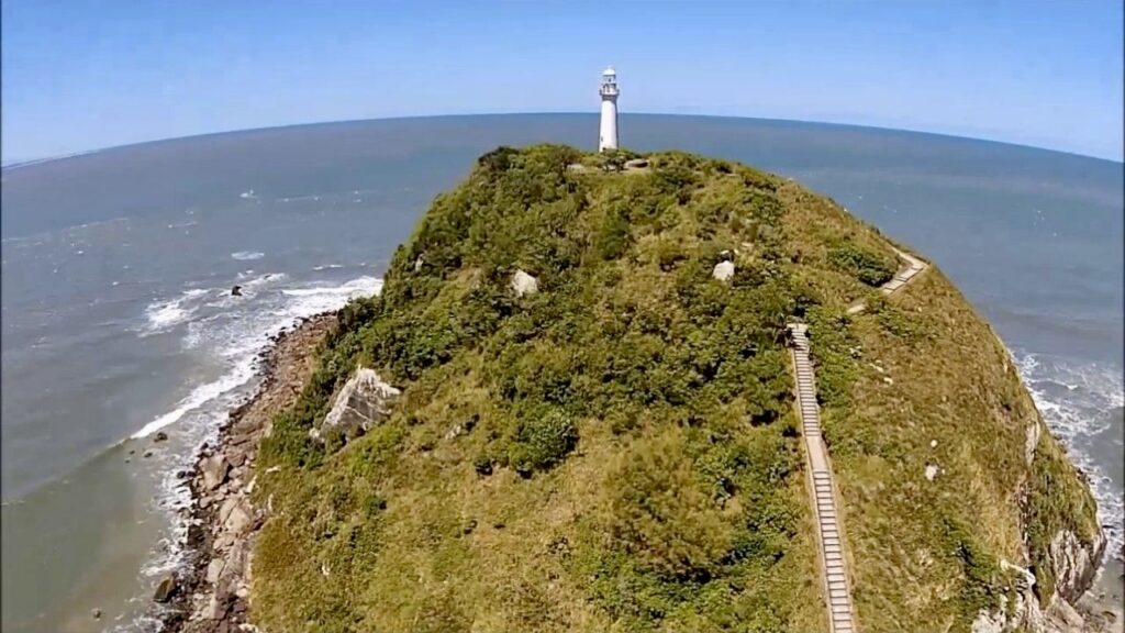 Scenic view of Farol das Conchas atop a lush hill on Ilha do Mel, Brazil, with a winding staircase leading up to the historic lighthouse.