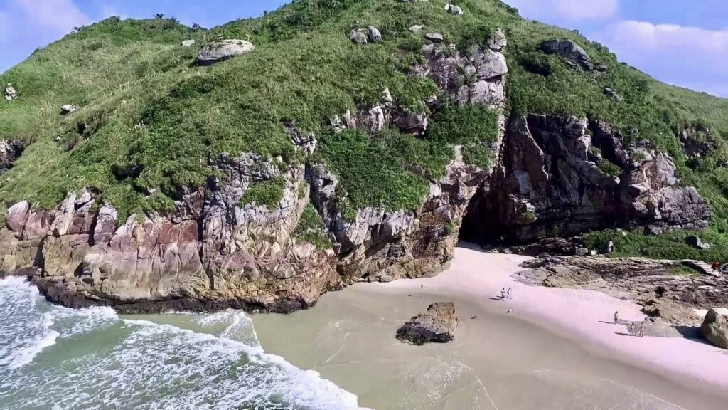 Entrance to Gruta das Encantadas on Ilha do Mel, Brazil, with rugged rock formations and ocean waves gently lapping at its base."
