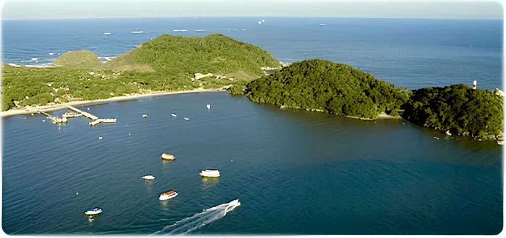 A breathtaking aerial view of Encantadas on Ilha do Mel, showcasing boats floating on crystal-clear waters, with lush green hills in the background.