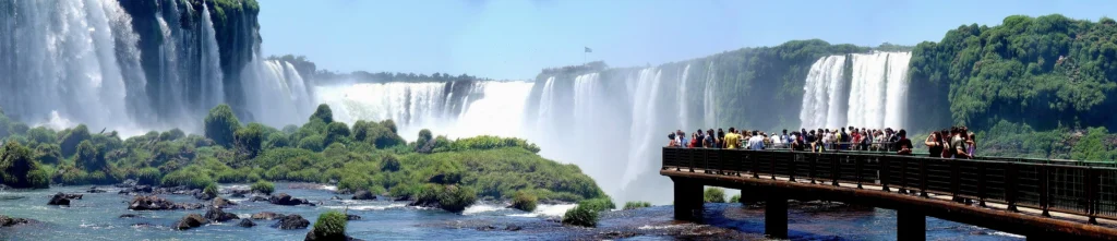 Visitors on a scenic walkway taking in the breathtaking view of Iguazu Falls surrounded by lush rainforest