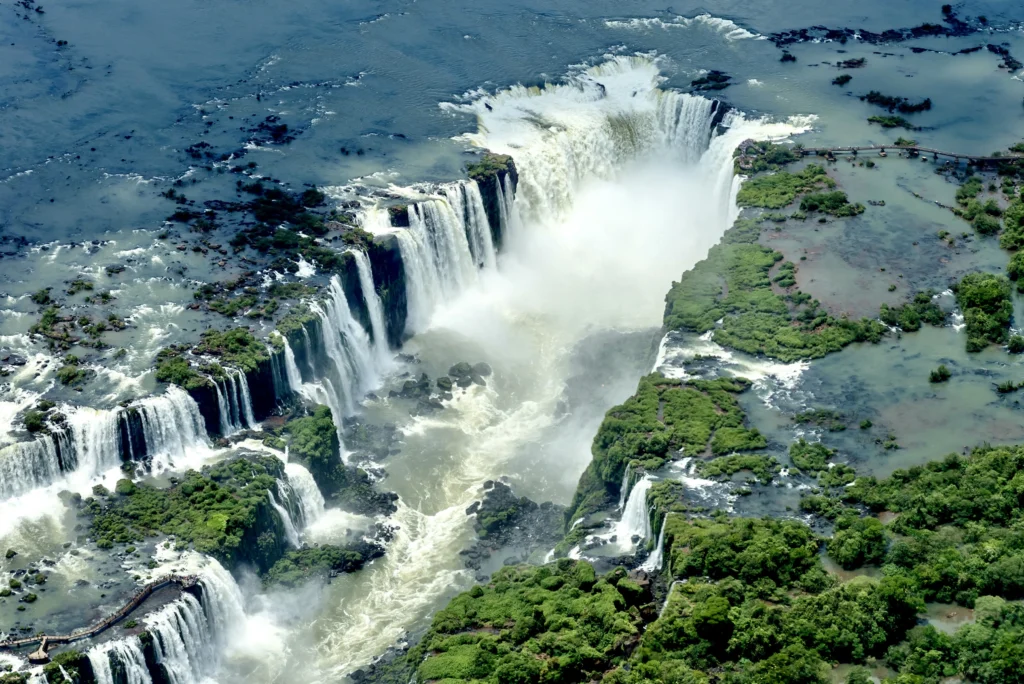 A panoramic view of Iguazu Falls cascading through lush rainforest on the Brazilian side, showcasing the natural wonder's power and beauty.