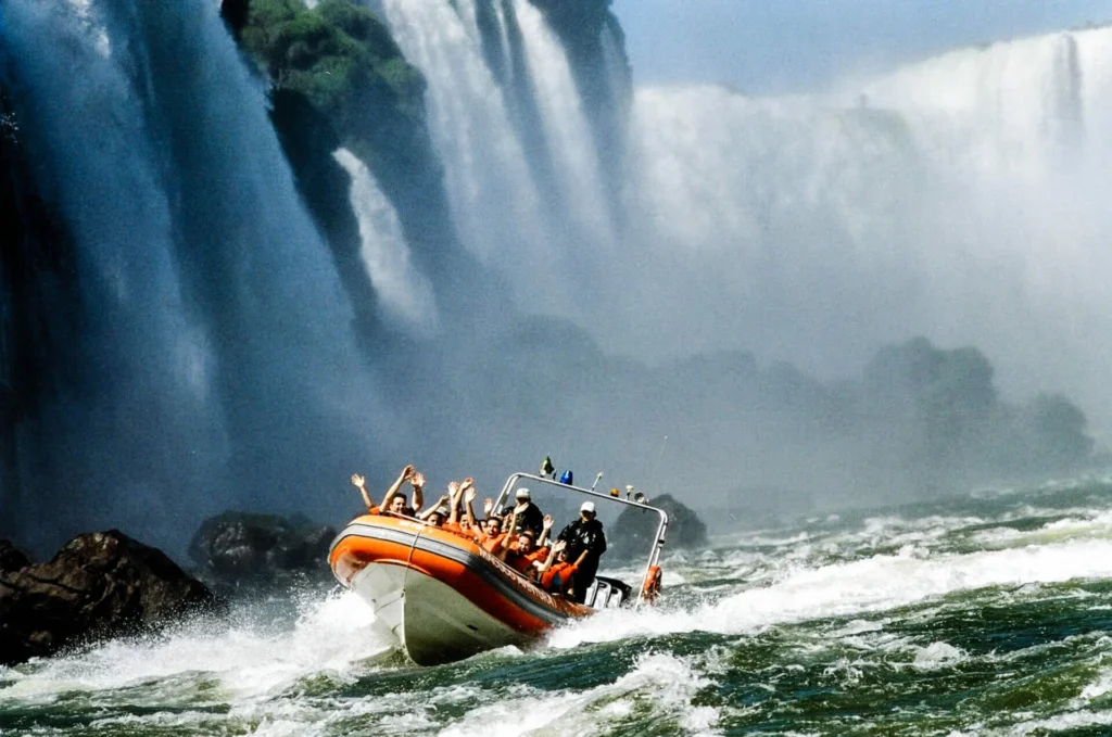 Tourist boat from the Macuco Safari approaching the base of Iguazu Falls, surrounded by mist and powerful cascades.